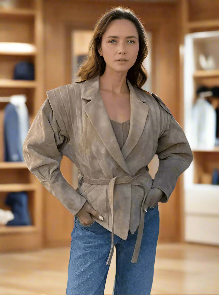 Woman wearing Maria chic suede jacket with belt, standing outdoors by a fence, showcasing stylish and comfortable fashion.